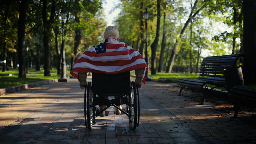 Military woman in park uses wheelchair wrapped in American flag, patriotic