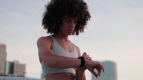 A young woman checks her fitness tracker during her workout on a city rooftop at sunset. She is focused and determined. - Powered by Shutterstock - Get 15% off with code: PIKWIZARD15