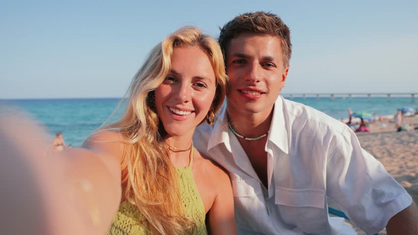 A cheerful couple captures a perfect selfie at the beach, radiating joy and excitement on a beautiful day. The coastline glimmers under the sun as they create lasting memories with laughter and smiles