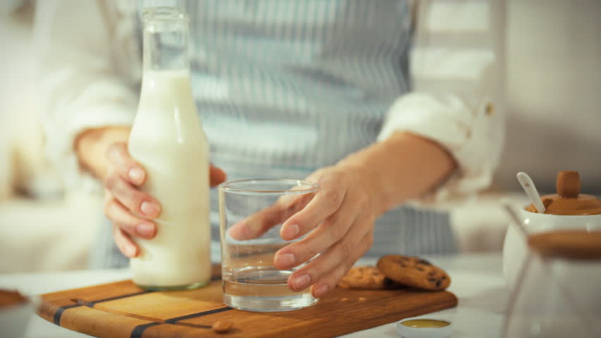 A person is carefully pouring fresh milk into a glass, preparing a delicious snack of cookies. This moment is taking place in a warm kitchen, filled with inviting aromas and a cozy ambiance