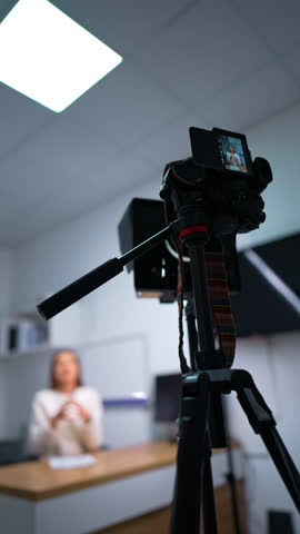 Emotional woman speaks to camera gesturing with hands. Low angle view at the camera on tripod shooting a lady. Blurred backdrop. Vertical video.