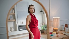 Elegant woman admiring dress in modern living room. Stylish lady posing in red gown reflected in large mirror at contemporary interior. Confident fashion brunette enjoy luxurious outfit in apartment. - Powered by Shutterstock - Get 15% off with code: PIKWIZARD15