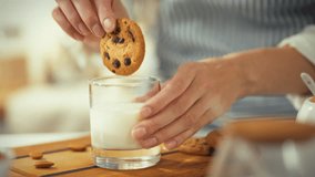 A person dips a chocolate chip cookie into a glass of milk in a bright kitchen. The atmosphere is warm and inviting, suggesting a moment of comfort and enjoyment - Powered by Shutterstock - Get 15% off with code: PIKWIZARD15