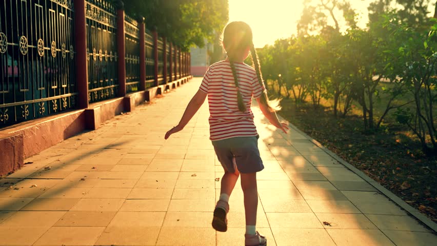 Girl kid runs along sidewalk on street sun. Children dream, happiness concept. Joyful little girl runs at sunset in city park in spring. Superhero girl plays dreams of flying. Active happy child play