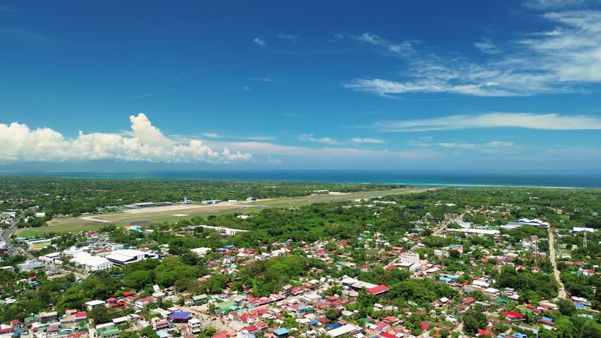 Drone footage capturing an aircraft approaching the runway at Puerto-Princesa International Airport, surrounded by city rooftops and tropical greenery in Palawan.