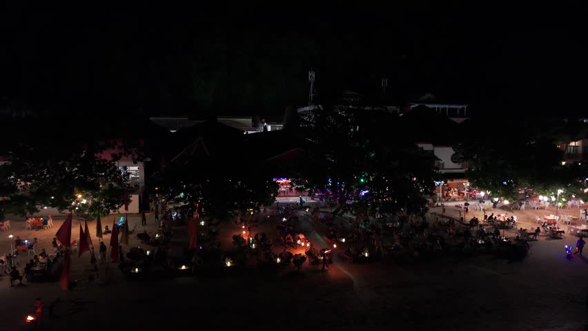 Tropical evening at beachside restaurant with tourists enjoying dinner while fire dancer performing mesmerizing routine against dark oceanic backdrop on gili trawangan island in indonesia