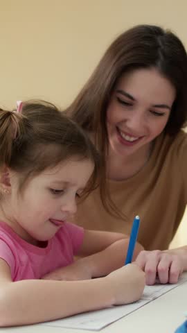 Happy brunette girl teaching homework with her little daughter child at home