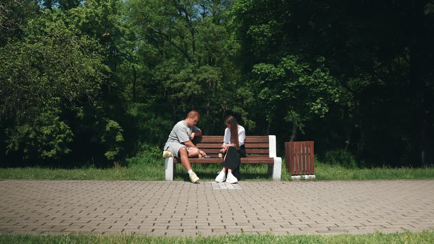 In a serene park, a young couple shares a joyful afternoon playing checkers on a wooden bench, laughing and bonding over their love for the game, surrounded by lush greenery