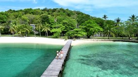 Couple strolls hand in hand along a wooden pier leading to the tranquil waters of Koh Kham Island Thailand. Lush greenery and soft sand surround this tropical paradise, offering a perfect escape. - Powered by Shutterstock - Get 15% off with code: PIKWIZARD15