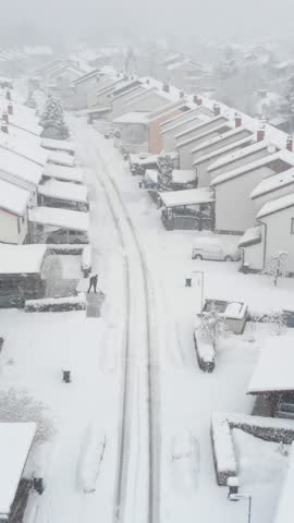 AERIAL: Unrecognizable person shoveling their driveway in the idyllic suburban neighborhood during a snowstorm. Flying above the empty streets of suburbia covered in the pristine freshly fallen snow.