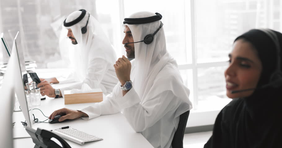 Group of Arab customers services employees sitting at desk in modern office, assist to clients remotely, provide detailed help by videocall or chat. Customer care, workflow of telemarketing department