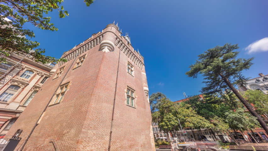 Renaissance dungeon clock tower and classical brick facade of the Capitole timelapse hyperlapse, city hall of Toulouse, France, surrounded by trees in Charles de Gaulle Square under a blue cloudy sky