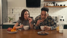 Multicultural couple having breakfast at the kitchen table. They dip cookies into milk and eat, enjoying a light and cheerful morning together. - Powered by Shutterstock - Get 15% off with code: PIKWIZARD15