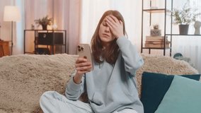 Upset young Caucasian woman sitting on sofa couch disappointed looking at smartphone and placing one hand on forehead expressing deep disappointment due to bad news or losing game. Adult girl at home. - Powered by Shutterstock - Get 15% off with code: PIKWIZARD15