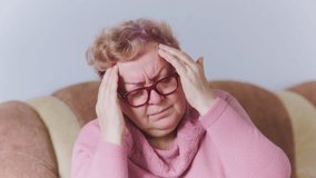A woman sits on a sofa, visibly distressed with a headache. She gently massages her temples while trying to find relief. This moment shows the challenges of coping with headaches at home. - Powered by Shutterstock - Get 15% off with code: PIKWIZARD15