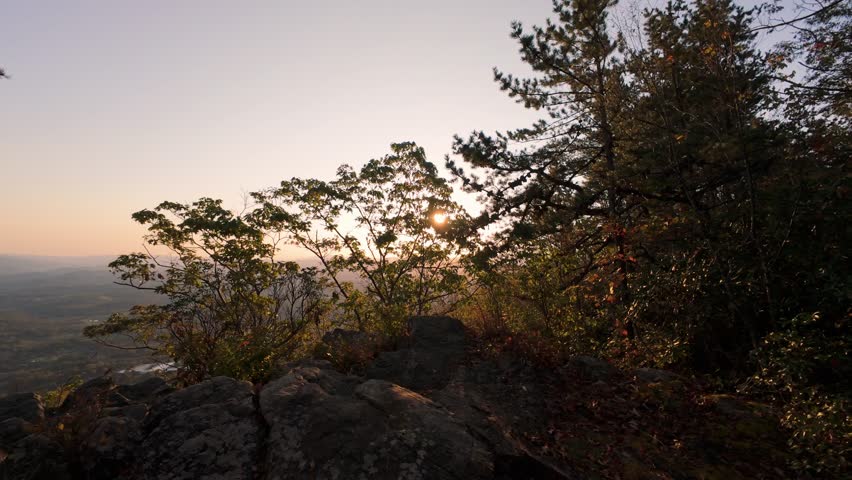 Sunlight peeks through trees on rocky forest ridge at golden hour, with distant valley views Sunset Through Trees on Rocky Forest Overlook sunlight peeks rock forest golden hour