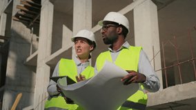 Multiethnic engineers discussing work at construction and making plan. Team of male and female working in safety helmets with building in background. Coworkers talking with drawing and tablet in hands - Powered by Shutterstock - Get 15% off with code: PIKWIZARD15