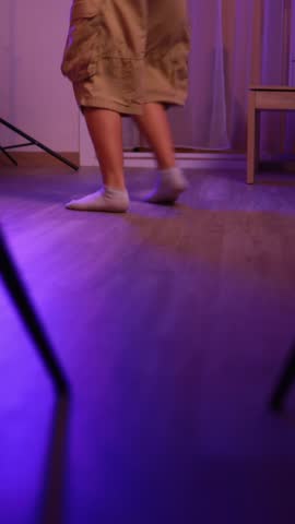 Energetic dancer showcasing breakdancing skills in a room illuminated with purple light, moving rhythmically and transitioning through various poses