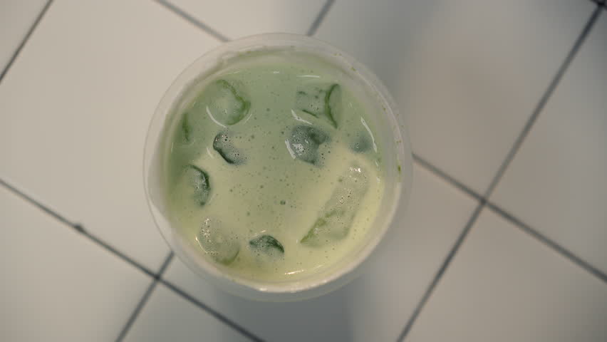 Top down tabletop view of iced tea or coffee with matcha, which a girl hand put in straw and stirs it.