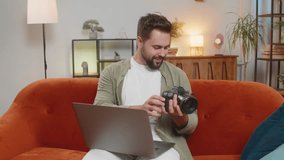 Portrait of happy young Caucasian brunette man photographer on sofa couch holding digital camera looking at screen, choosing photos for editing while sitting in front of laptop computer at home room. - Powered by Shutterstock - Get 15% off with code: PIKWIZARD15