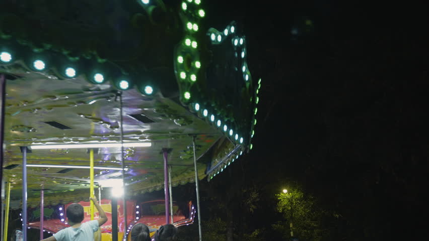 Panoramic view of a carousel with many families and children enjoying a relaxing ride in a park at night