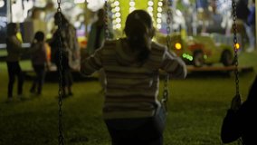 Two girls swinging on the playground equipment in a park lit with Christmas lights, surrounded by family and friends - Powered by Shutterstock - Get 15% off with code: PIKWIZARD15