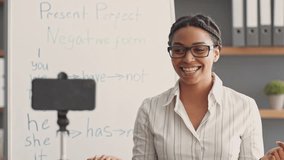 An African American woman conducts an online tutoring session, teaching English grammar. She uses a smartphone to connect with her students while standing by a whiteboard. - Powered by Shutterstock - Get 15% off with code: PIKWIZARD15