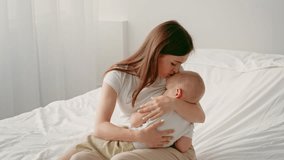 A mother tenderly holds her baby on a bed in a softly lit room. The child seems relaxed and content. This warm moment highlights the bond between them in their comfortable home environment. - Powered by Shutterstock - Get 15% off with code: PIKWIZARD15