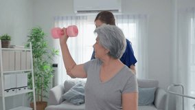 Asian senior mature woman doing physiotherapist with support from nurse. Elderly older female patient using dumbbells workout exercise to improve mobility and strength with caregiver at nursing home. - Powered by Shutterstock - Get 15% off with code: PIKWIZARD15