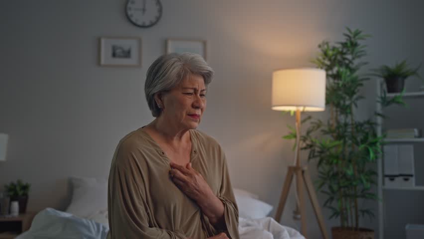 Asian senior elderly depressed woman sitting alone in bedroom at home. Attractive mature grandmother feeling sad, lonely and frustrated with life problem think of money debt, budget loss, bankruptcy.