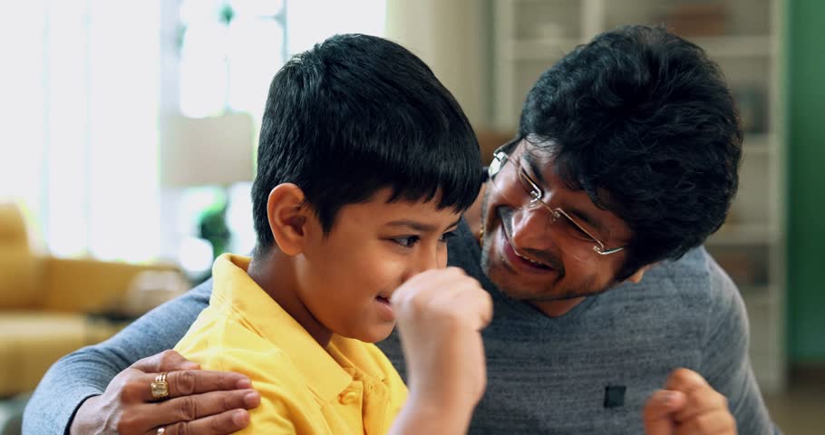 Indian Asian father and young kid celebrating success together at a study table with a laptop, checking results in a modern lavish home, expressing joy and achievement in an educational setting