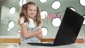 Cute girl using laptop programing software while looking at camera with confident to celebrate successful project. Pretty child coding system while smiling at camera proudly in Stem class. Erudition. - Powered by Shutterstock - Get 15% off with code: PIKWIZARD15