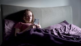 A woman lies in bed, browsing her phone in a calm and relaxed setting. - Powered by Shutterstock - Get 15% off with code: PIKWIZARD15
