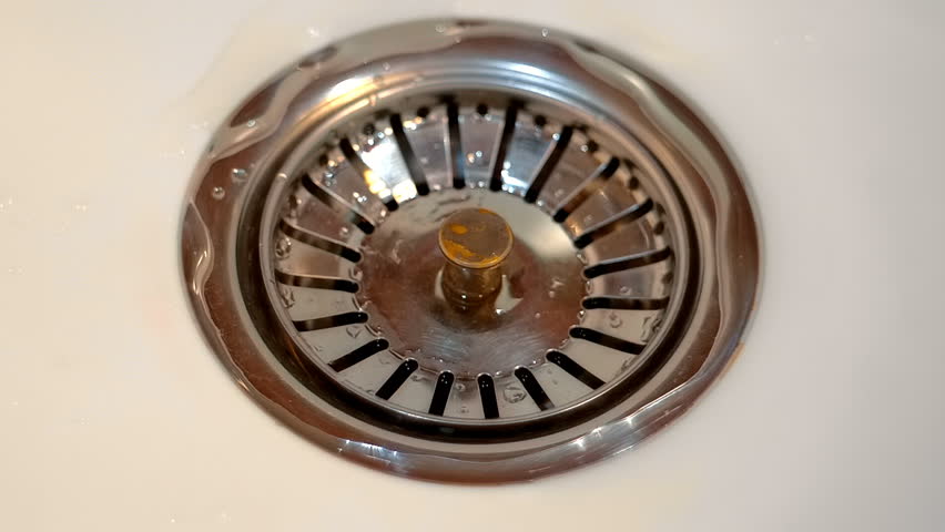 A stream of water flows into a shiny chrome drain in a white sink. Closeup. Macro. Slow mo, slow motion, high speed camera, 250fps