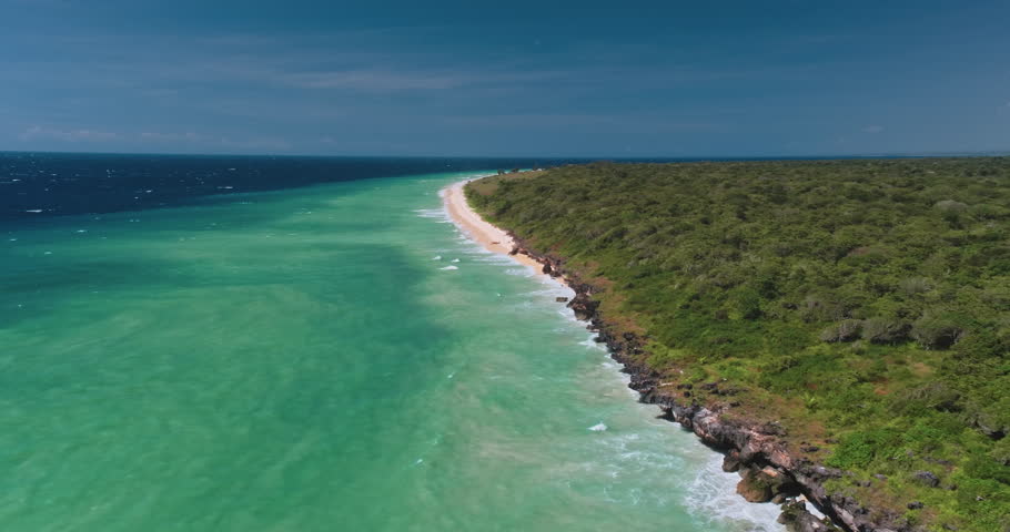 Breathtaking aerial view capturing turquoise ocean waves crashing on pristine white sand beach, bordered by lush green vegetation on Sumba Island, Indonesia