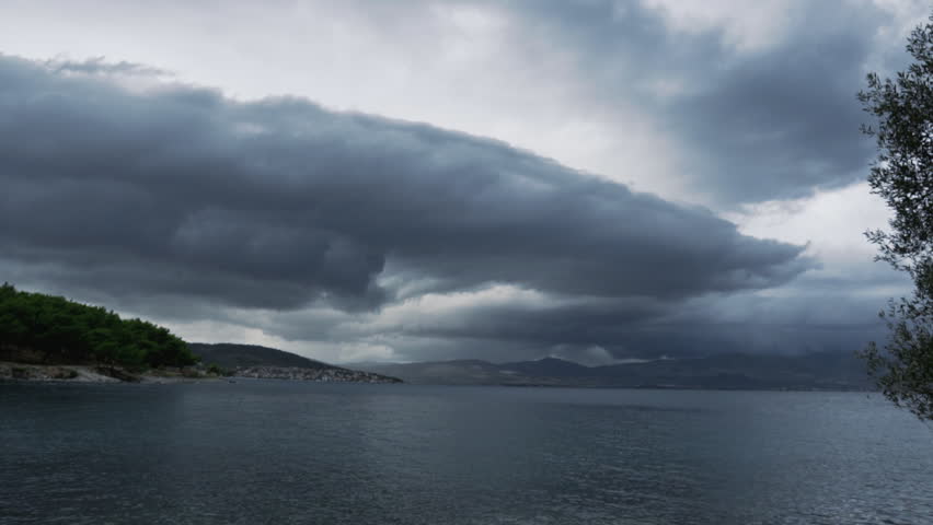 Timelapse of dramatic storm clouds gathering over coastal landscape. Squalls, gusts of wind visible on water. Dense greenery on rugged shoreline. Wide angle. Croatia.