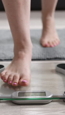 Vertical Video of Girl Legs Step On Bathroom Scale. Woman On Scales Measure Weight. Human Barefoot Measuring Body Fat Overweight. Slim Woman Checking BMI Weight Loss. Feet Standing Weighing Scales