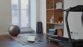 Interior of home gym with treadmill, yoga mat, laptop, dumbbells, exercise ball, water bottle and shelves of wellness equipment - Powered by Shutterstock - Get 15% off with code: PIKWIZARD15
