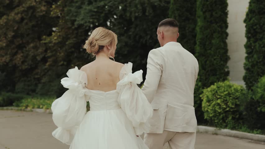 Rear view, romantic wedding couple in elegant attire walking holding hands