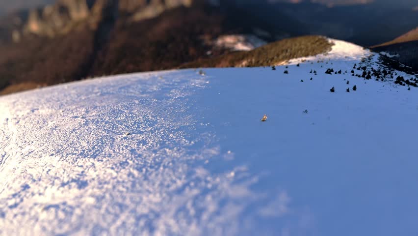 Aerial view in high-mountain winter landscape, forward movement focusing on rocky peak with tilt-shift effect