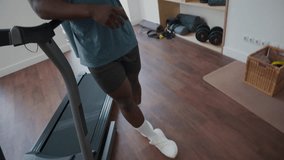 Tilt up shot of athletic Black man standing by treadmill in home gym and speaking on mobile phone while resting after workout - Powered by Shutterstock - Get 15% off with code: PIKWIZARD15