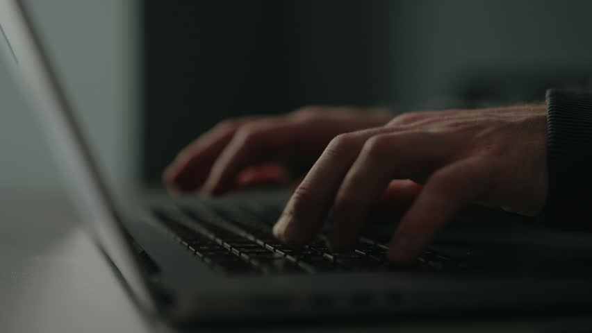 Close-up of freelancer male remote working from home office, developing software solutions, sitting at table by window in dark room. Concept of remote job, technology, people. Shooting in slow motion.