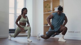 Muscular Black fitness instructor explaining how to perform lunge stretch while leading personal workout with young woman in modern minimalist gym - Powered by Shutterstock - Get 15% off with code: PIKWIZARD15