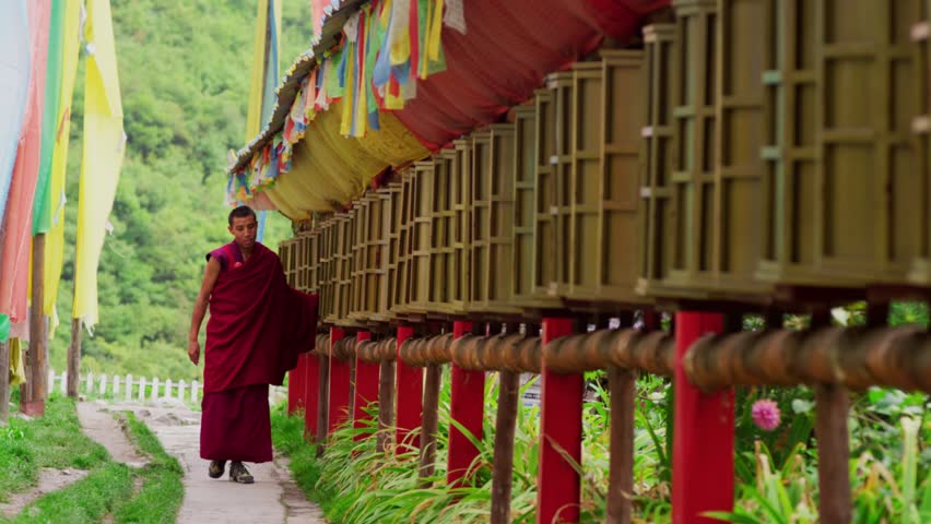 On the road to a temple on the hillside of Jiuzhaigou in Sichuan, a Tibetan monk in a crimson robe walks by and turns a long row of prayer wheels hung with colorful flags.