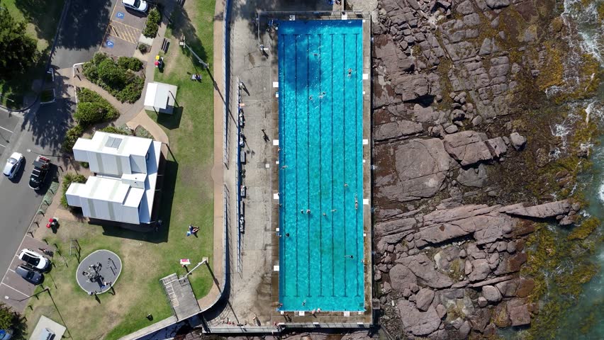 Top down ascend of Shellharbour Ocean Pool surrounded by rocky coast and breaking waves