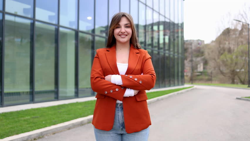 Young businesswoman smiling with crossed arms in front of modern office building