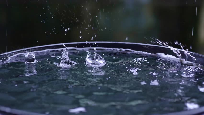 Rain drops falling into barrel, collecting water, splashing close up