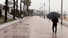view from behind of a man with an umbrella walking along the beach promenade during the rain - Powered by Shutterstock - Get 15% off with code: PIKWIZARD15