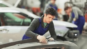 Man auto mechanic performs car body work in auto repair shop. Male auto mechanic handle polishes vehicle body parts, performs minor repairs, eliminating deformations, hiding flaws.  - Powered by Shutterstock - Get 15% off with code: PIKWIZARD15