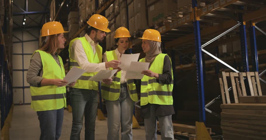 Warehouse workers reviewing paperwork. Diverse team of employees discussing logistics and inventory in storage facility.